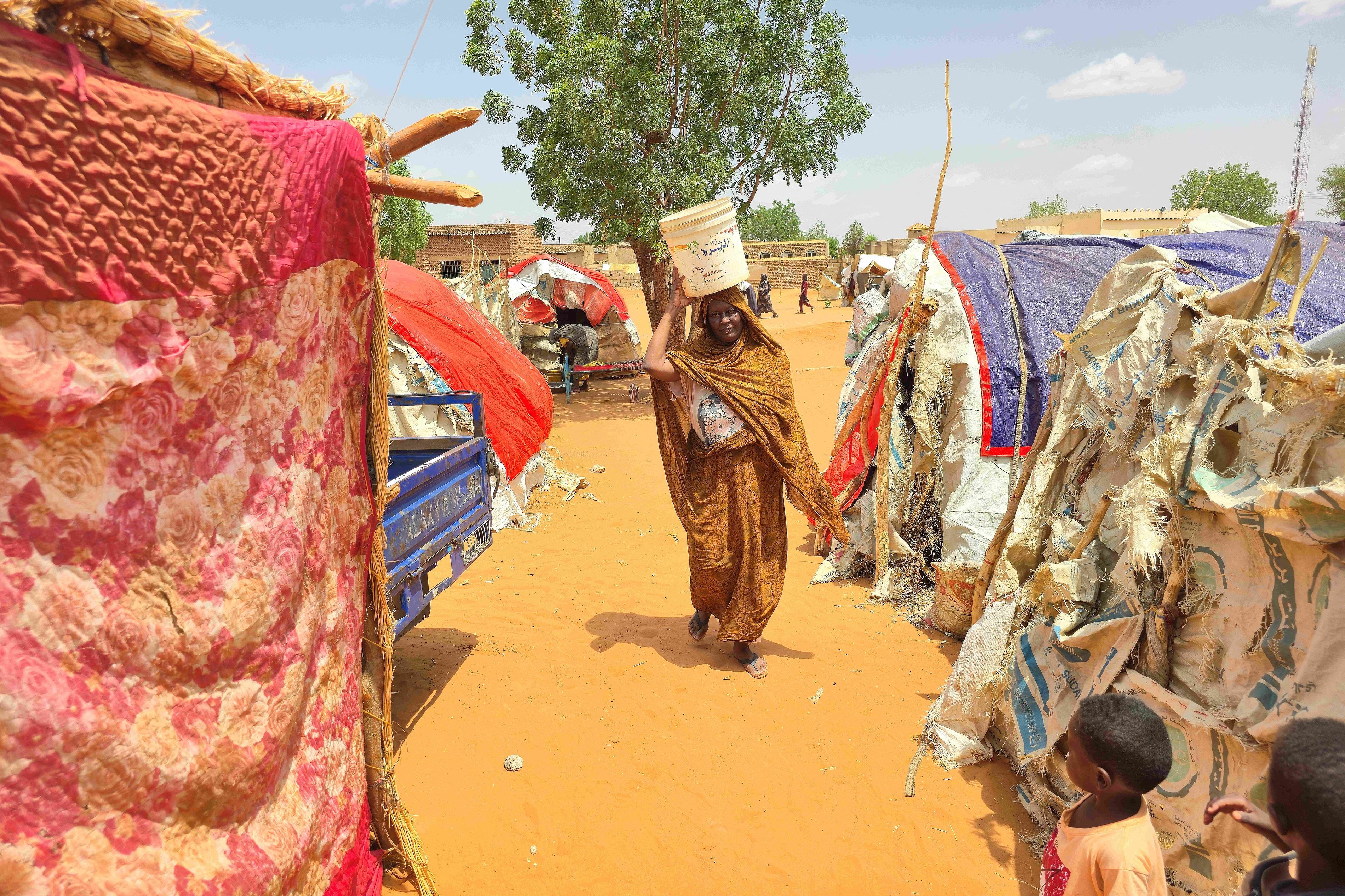 AFP via ANP-A Sudanese woman walks as she carries a plastic canister in al-Rahmaniyah camp for displaced people, near the city of El-Obeid in the southern Kordofan region, on June 25, 2026.jpg