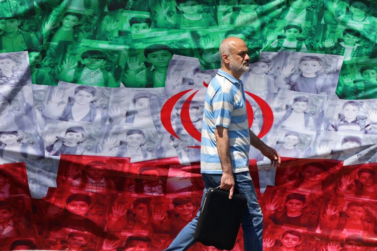  Een man loopt op 29 april 2026 langs een Iraanse vlag die langs de weg in Teheran is opgehangen, met daarop afbeeldingen van kinderen die op de eerste dag van de oorlog zijn omgekomen bij een vermeende Amerikaans-Israëlische raketaanval op een school.