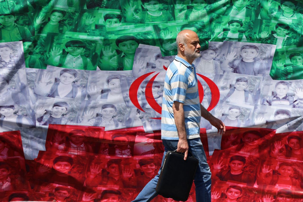  Een man loopt op 29 april 2026 langs een Iraanse vlag die langs de weg in Teheran is opgehangen, met daarop afbeeldingen van kinderen die op de eerste dag van de oorlog zijn omgekomen bij een vermeende Amerikaans-Israëlische raketaanval op een school.